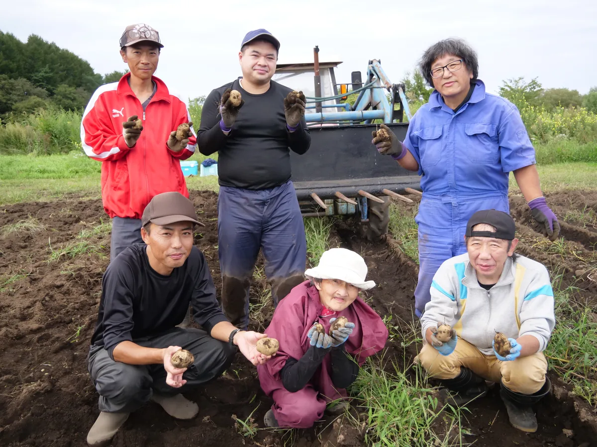 農機の前に集まり、じゃがいも畑で収穫したじゃがいもを手に持つ6人