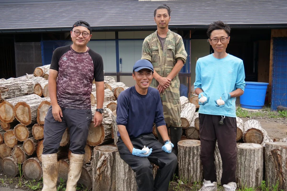 作業場の前に集まり、二人がにんにくを手に持つ四人