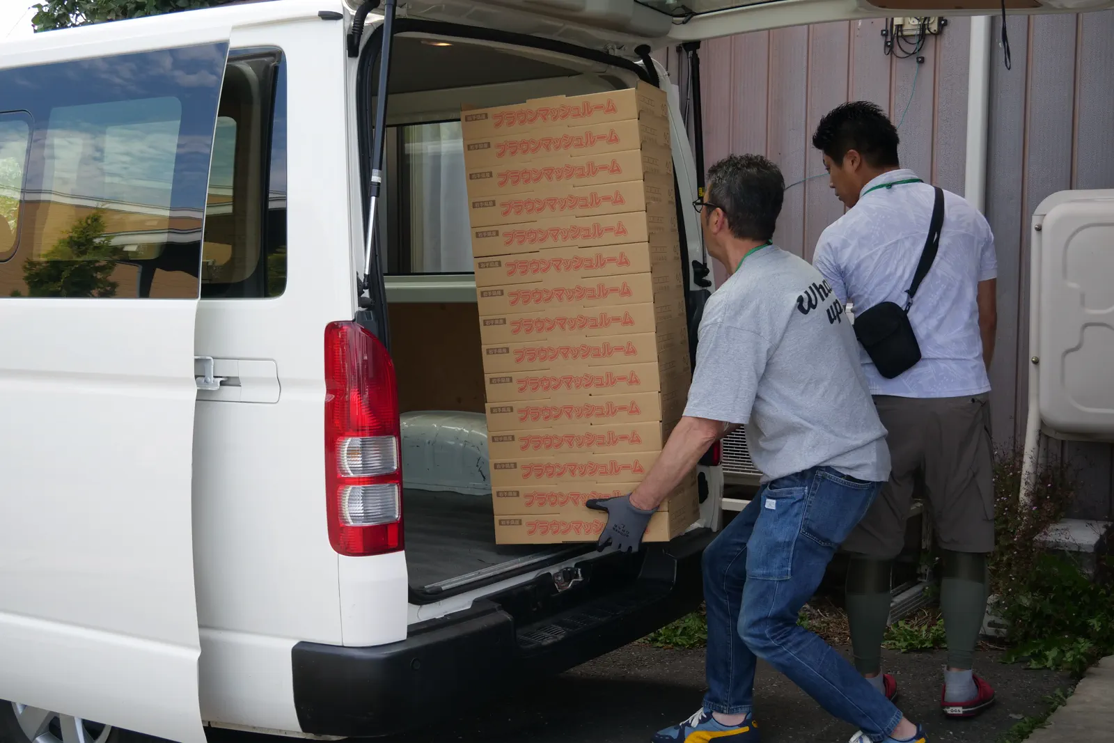 二人で板状の荷物を車両へ運ぶ様子